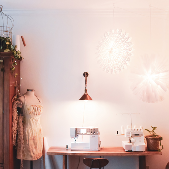 Meg's sewing studio with a narrow side table used for a sewing machine and serger under a small hanging light, with a wardrobe for scraps nearby
